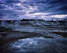 The many geysers of the Norris Geyser Basin add their own clouds to those of the pending storm.  Well after sunset, the red glow of the sun can barely be seen to illuminate this other worldly landscape in Yellowstone National Park, WY.